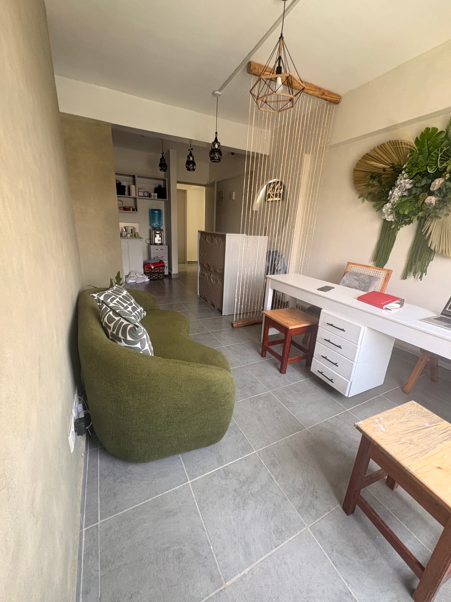 Kiki's mini spa lounge with a green velvet sofa, woven rope screen and neon signage